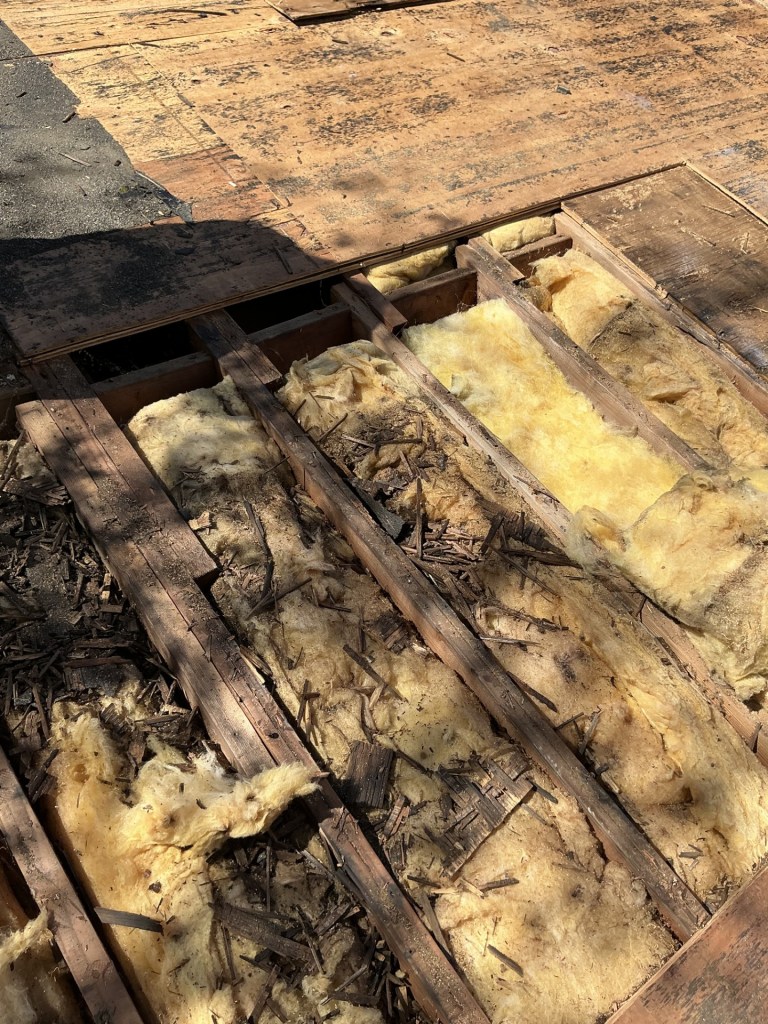 Removed cathedral ceiling decking showing compressed insulation against sheathing with no airspace—re-engineered for proper ventilation.